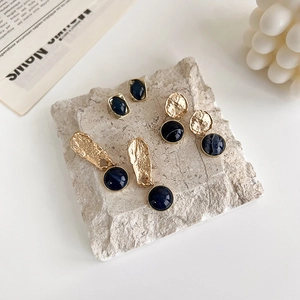 Close-up of three vintage Klein blue and gold earrings on a textured stone surface