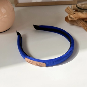 Detail of Klein blue velvet headband with handmade leather label on white surface