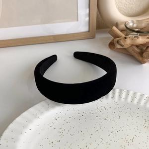 Detail shot of a black knitted padded headband resting on a textured white ceramic plate