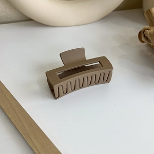 Détail d'une pince à cheveux rectangulaire marron mat posée sur une surface boisée épurée