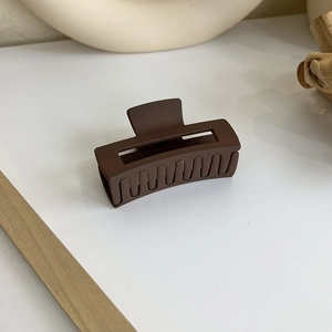 Gros plan d'une pince à cheveux rectangulaire creuse marron foncé mat sur fond blanc
