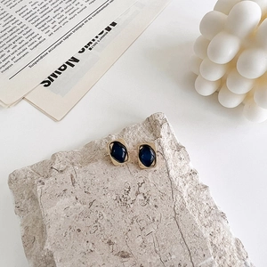 Detail of geometric gold earrings with blue resin inlay displayed on light stone plate