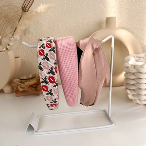 Three assorted pink fabric headbands displayed on a modern white metal minimalist stand