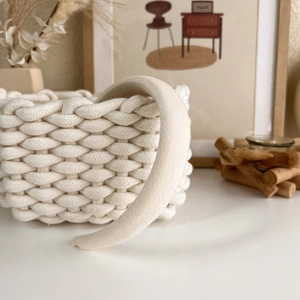 Close-up of a textured cream fabric headband displayed on a woven basket in a cozy setting