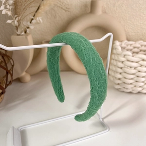 Close-up of green textured fabric headband with pleated detail on a white display stand