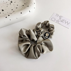 Elastico scrunchie in raso verde oliva con ciondolo a rosa dorata su sfondo bianco