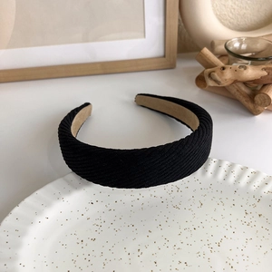 Detail of a black pleated wide headband on a ceramic plate with a textured fabric surface