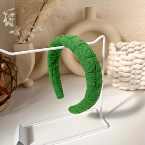 Detail shot of green quilted padded headband with rhombus stitching on a white stand