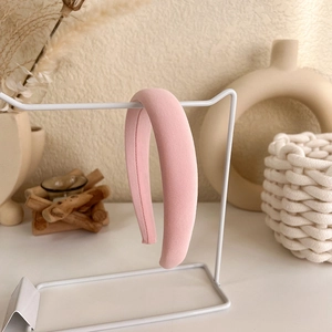 Detail view of a soft pink padded headband displayed on a minimalist white metal stand