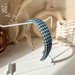 Close-up of green and blue checkered knitted headband hanging on a white metal stand