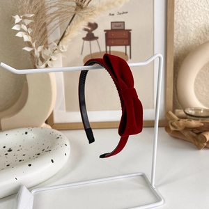 Détail d'un serre-tête vintage en velours rouge foncé avec un nœud 3D sur un support blanc