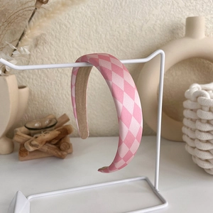 Close-up of pink and white checkered sponge headband on a white metal display stand