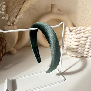 Detail of dark green padded satin headband featuring a handmade label on metal stand