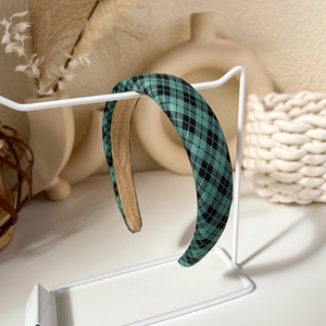 Detailed view of green argyle plaid headband on a white metal display stand