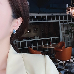 Klein blue rectangular enamel earrings with silver frame worn by a model in a cafe
