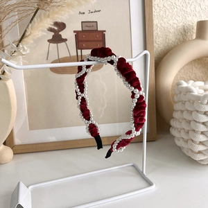 Détail d'un serre-tête en velours rouge avec perles blanches sur support d'exposition