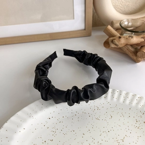 Close-up of black pleated PU leather headband with matte texture on a ceramic plate