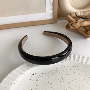 Detail of a thick black patent leather headband showing the khaki non-slip velvet lining