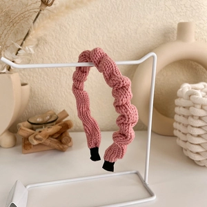 Detail of pink knitted headband with wave texture on a minimalist white display rack
