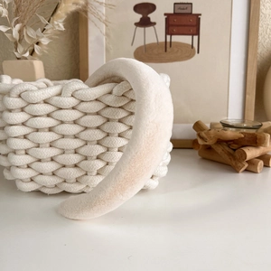 Detail of a plush cream-white headband resting on a woven basket in a warm minimalist setting