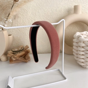 Detailed close-up of pink velvet padded headband on white display stand in a room