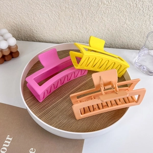 Close-up of three matte large square hair claws in yellow, pink and peach colors