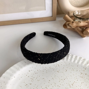 Detailed close-up of a black tweed headband with golden threads and a handmade label