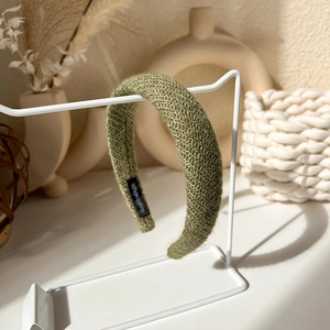 Detailed view of green knitted headband with handmade label on white display stand