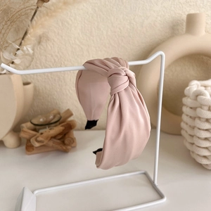 Detail of pink knotted wide headband with silk texture on a white display stand