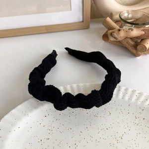 Detail of elegant black knitted headband with ruffled texture on a white ceramic plate