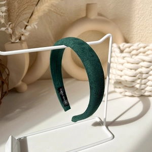 Detailed view of deep green padded headband with hand-made label on white metal stand