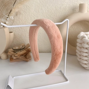 Detailed close-up of a plush pink padded headband hanging on a white metal rack stand