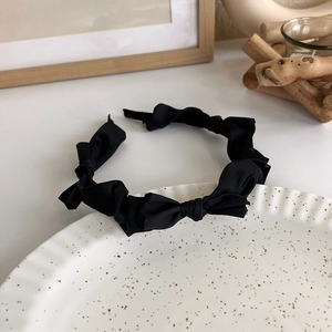 Detail of a black satin twist headband with an elegant bow on a decorative ceramic tray