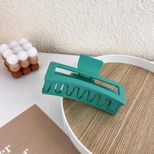 Detail of large matte dark green square hair claw clip on minimalist wooden background