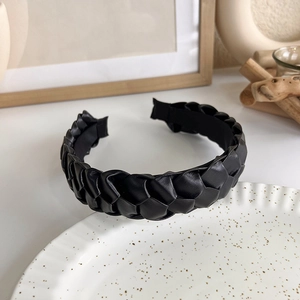 Detailed view of wide braided black faux leather headband on a minimalist ceramic plate