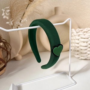 Detail of dark green knitted headband with heart ornament hanging on white stand