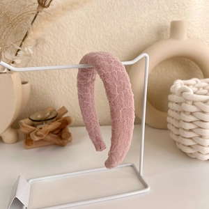 Detail of pink sponge headband with pleated lace texture on a minimalist stand