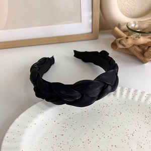 Detail view of black satin braided headband on decorative wooden and ceramic background