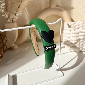 Detail view of a green padded headband with a black heart charm and Smile U woven label