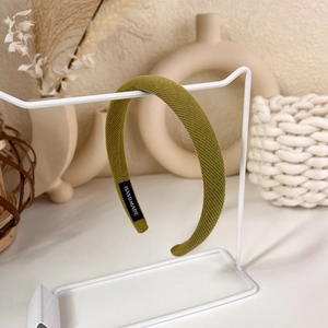 Detail view of grass green knitted headband with Handmade label on white stand