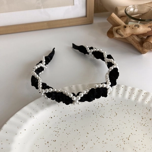 Close-up of black pleated fabric headband with woven pearls on a white porcelain plate