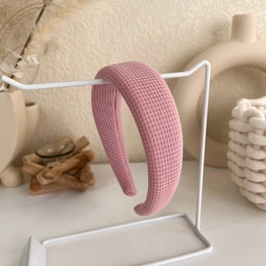 Detail shot of a pink waffle-textured padded headband hanging on a white metal display stand