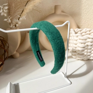 Detailed close-up of dark green handmade wool headband with woven texture on a white stand
