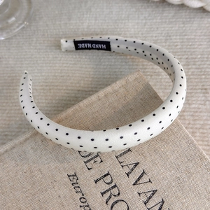 Detail showing white polka dot fabric headband with a black handmade woven label tag