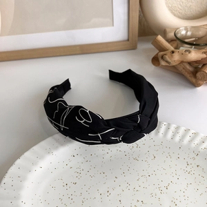 Close-up of black knot headband with white abstract face patterns on a ceramic plate
