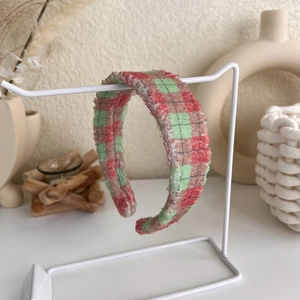 Detail of red and green plaid tweed headband with textured fringe on a display stand