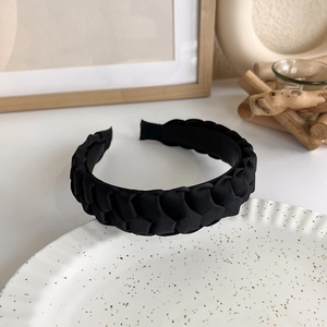 Detail view of a thick black knitted headband placed on a white ceramic plate
