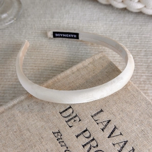 Close-up of beige satin wide headband featuring a black handmade woven label detail
