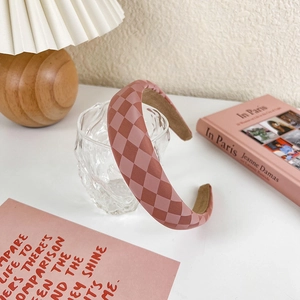 Close-up of pink checkerboard sponge headband leaning on a clear glass with soft lighting