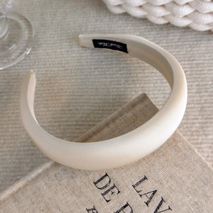 Close-up of a cream thick padded headband with a silk texture and Hand Made label